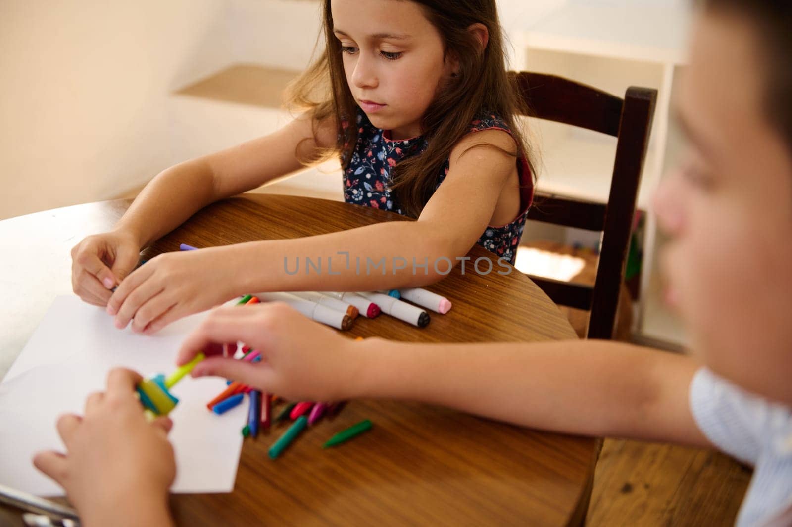 Young children sitting at a table focusing on coloring and crafting, showcasing childhood creativity.