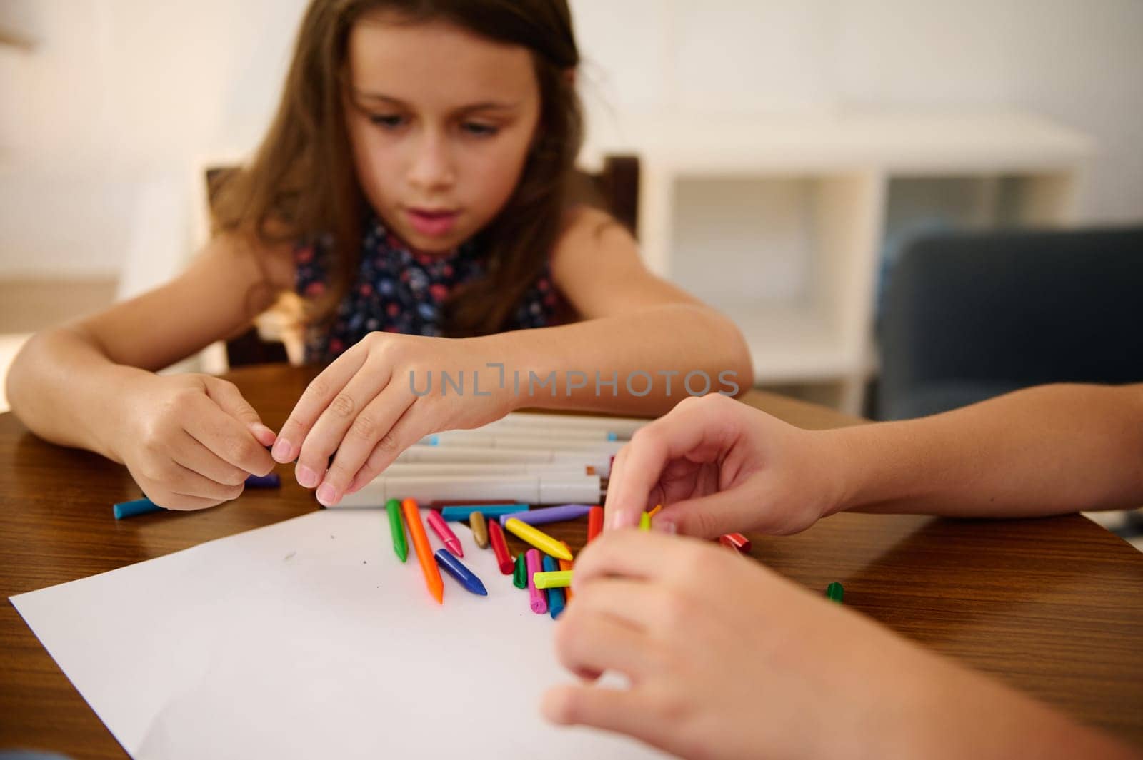 Two kids engaged in a creative activity using colorful crayons on a table indoors.