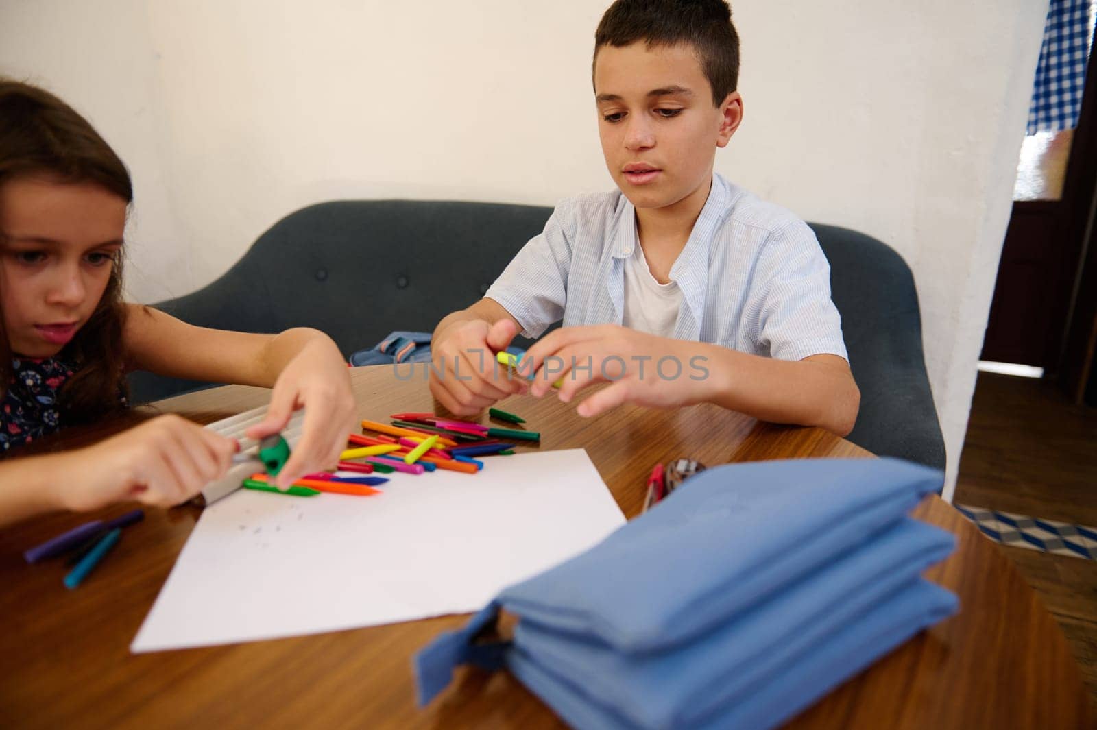 Two children engaging in an arts and crafts activity, using colorful crayons on paper. This indoor moment depicts creativity, focus, and youthful learning and expression at a wooden table.
