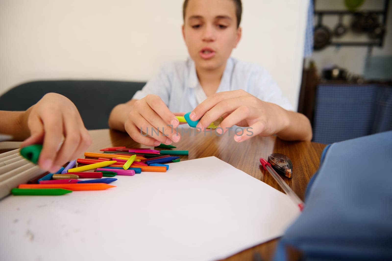 Boy arranging colored pencils while preparing a creative project on a wooden desk in a home setting.