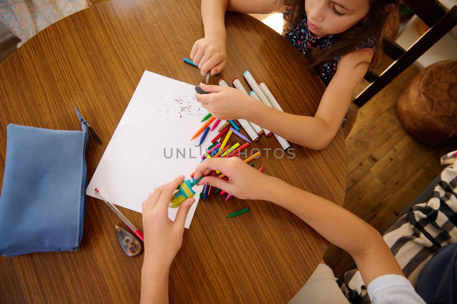 Two children are sitting at a wooden table, creating art with colorful markers and paper, capturing creativity and collaboration.