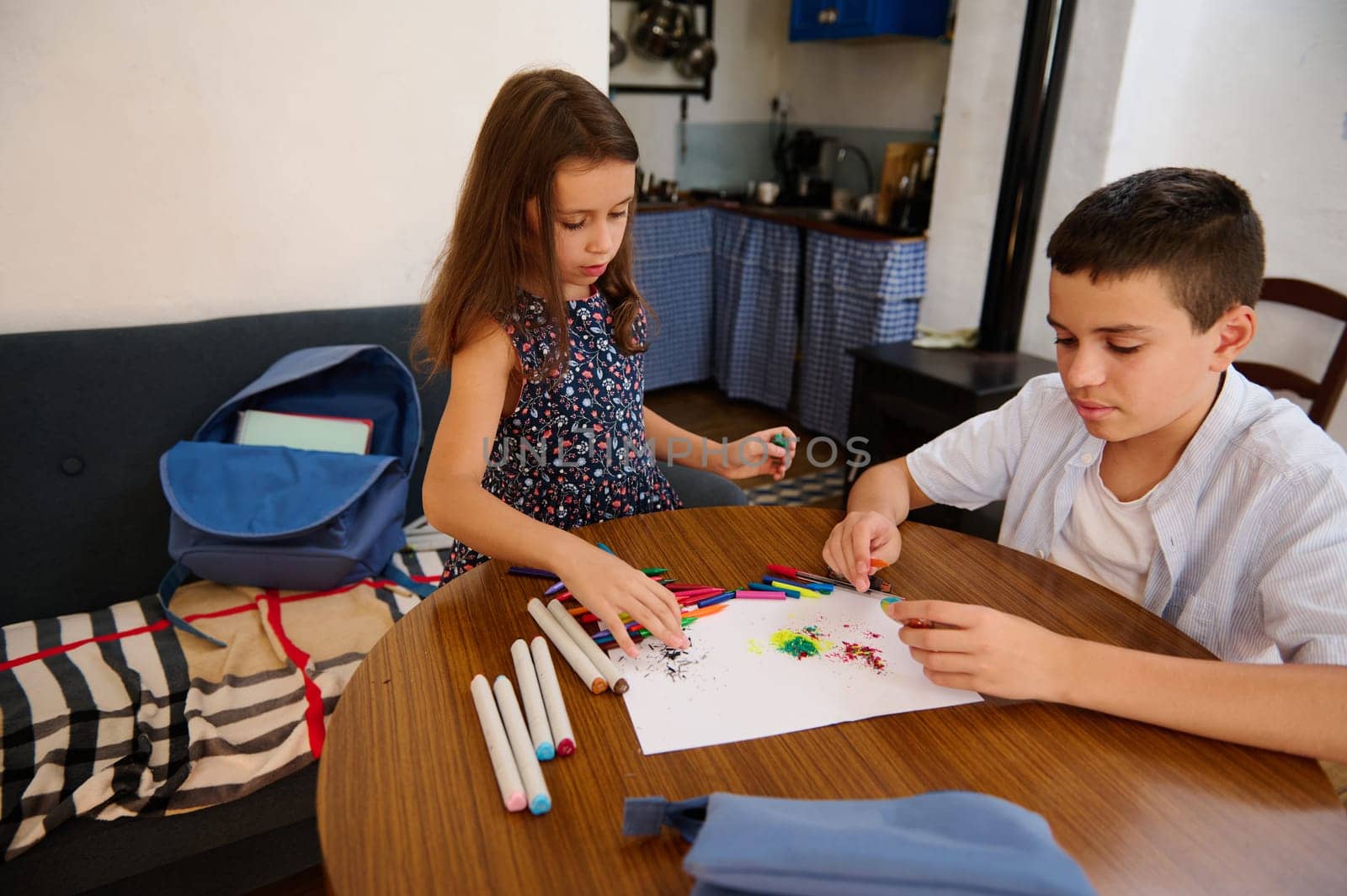 Two children engaging in creative art activities, crafting vibrant pictures on paper, enjoying a fun, hands-on moment. Backdrop shows a cozy interior setting, a school bag resting nearby.