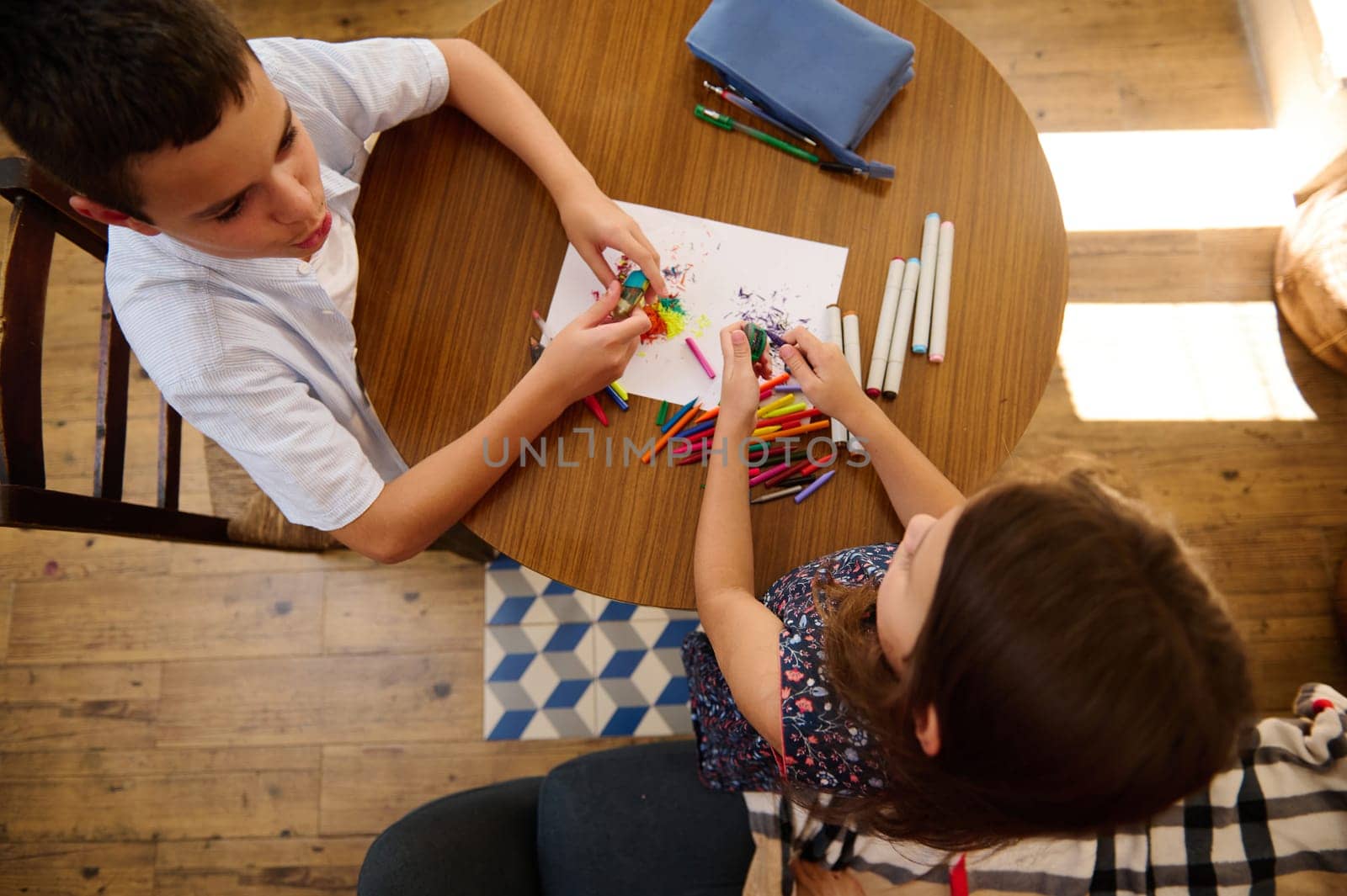 Two children sit at a table, surrounded by art supplies, sharing a moment of creative expression and childhood imagination.
