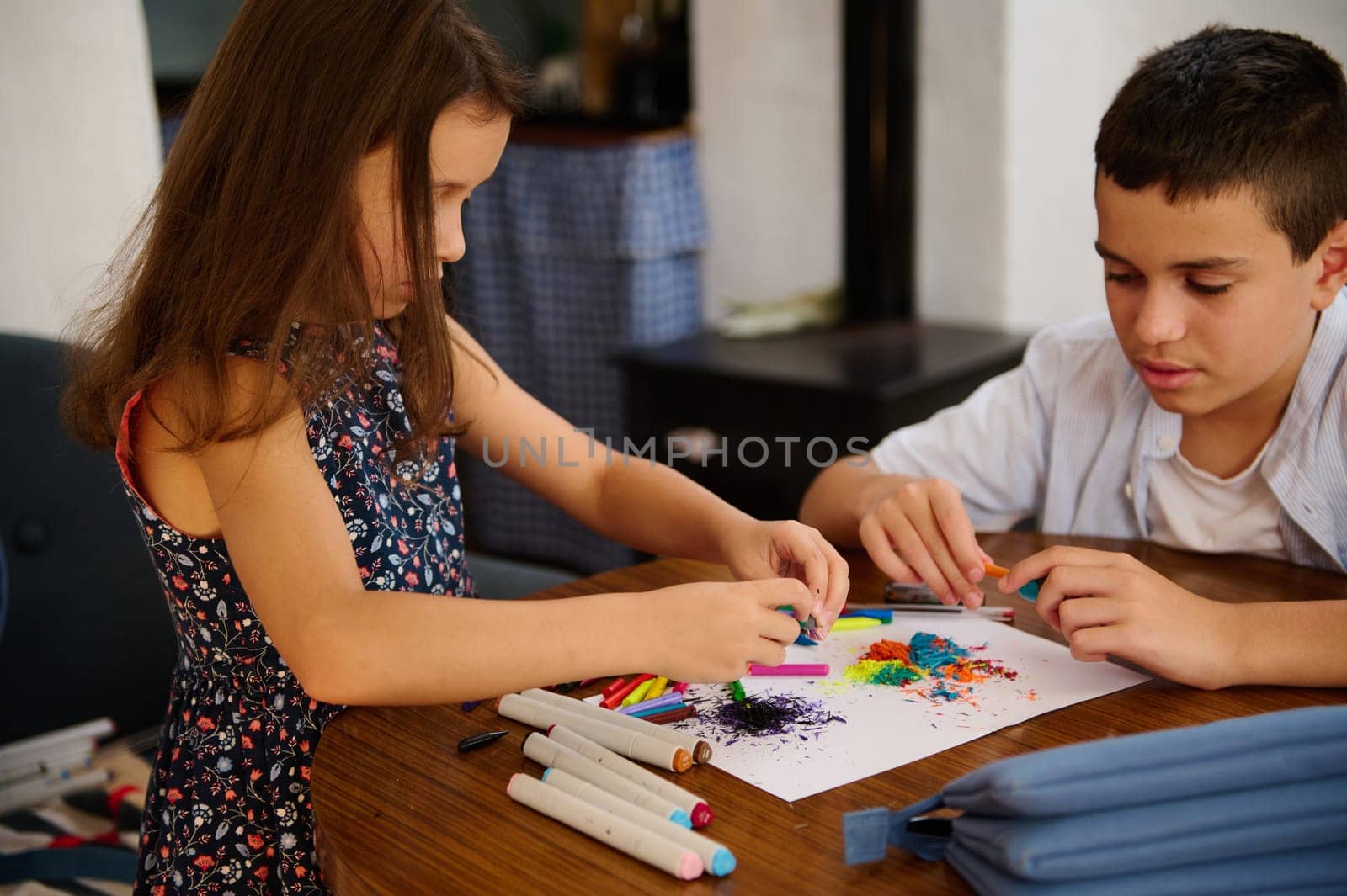 A young boy and girl creating art together using colorful markers and paper at a table.