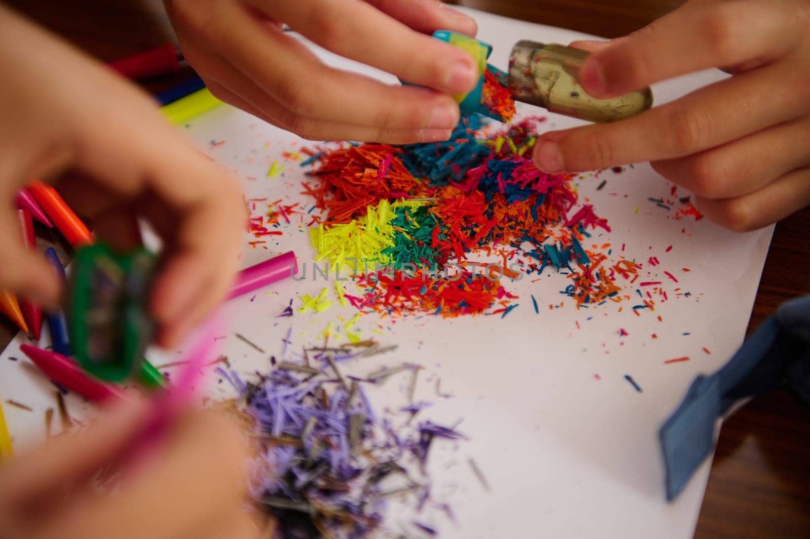 Close-up of hands shavings pencils, showcasing vibrant, multicolored pencil pieces, ideal for illustrating creativity, art concepts, or hands-on educational activities.