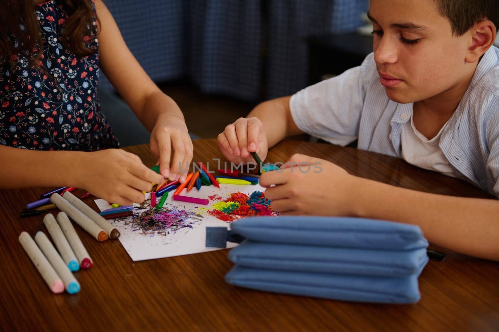 Two children focus on crafting art using colorful supplies on a wooden table, emphasizing creativity.