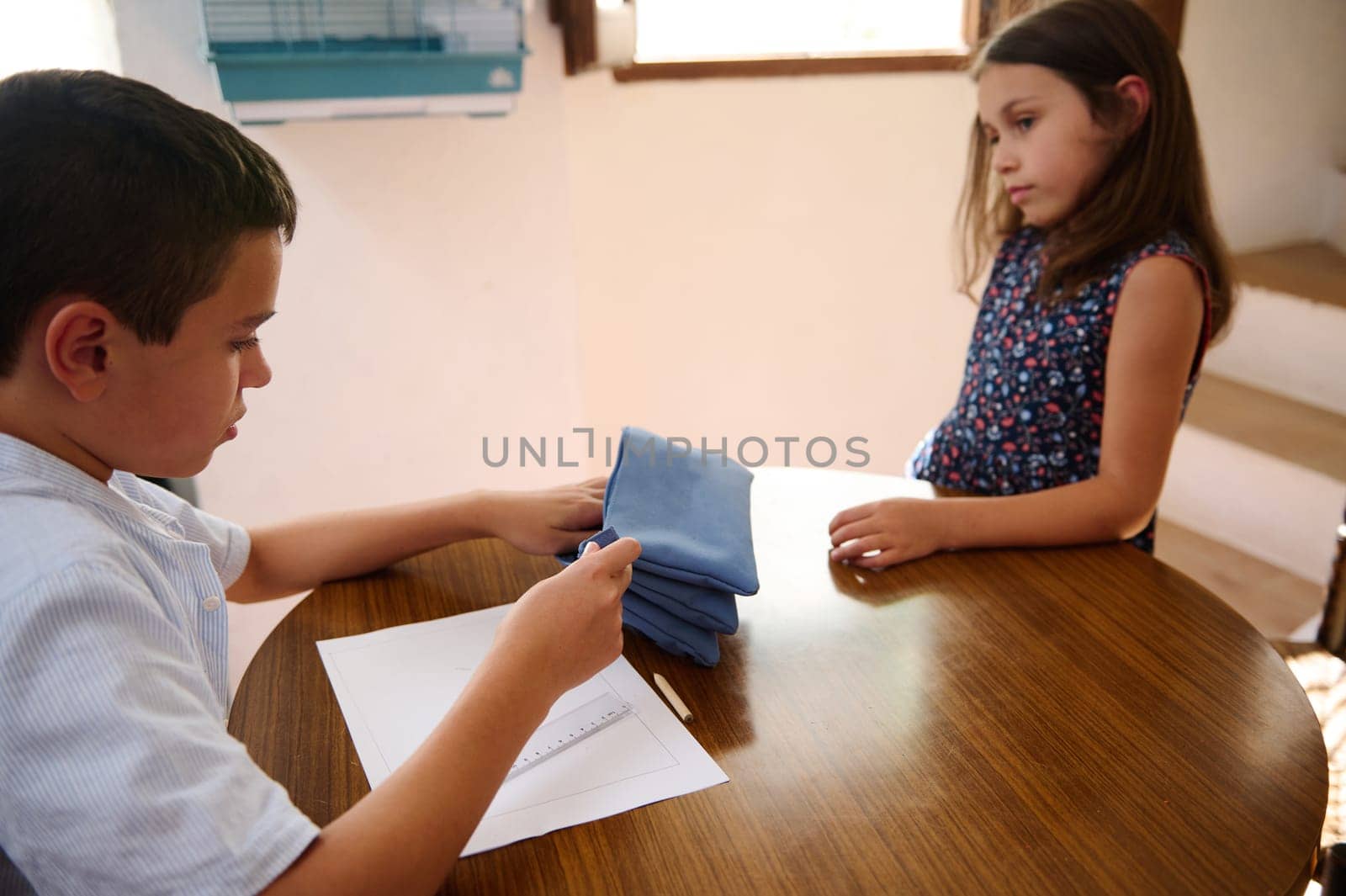 Two children collaborate on organizing items at home, showcasing teamwork and responsibility through a shared task at a wooden table in a sunlit room.