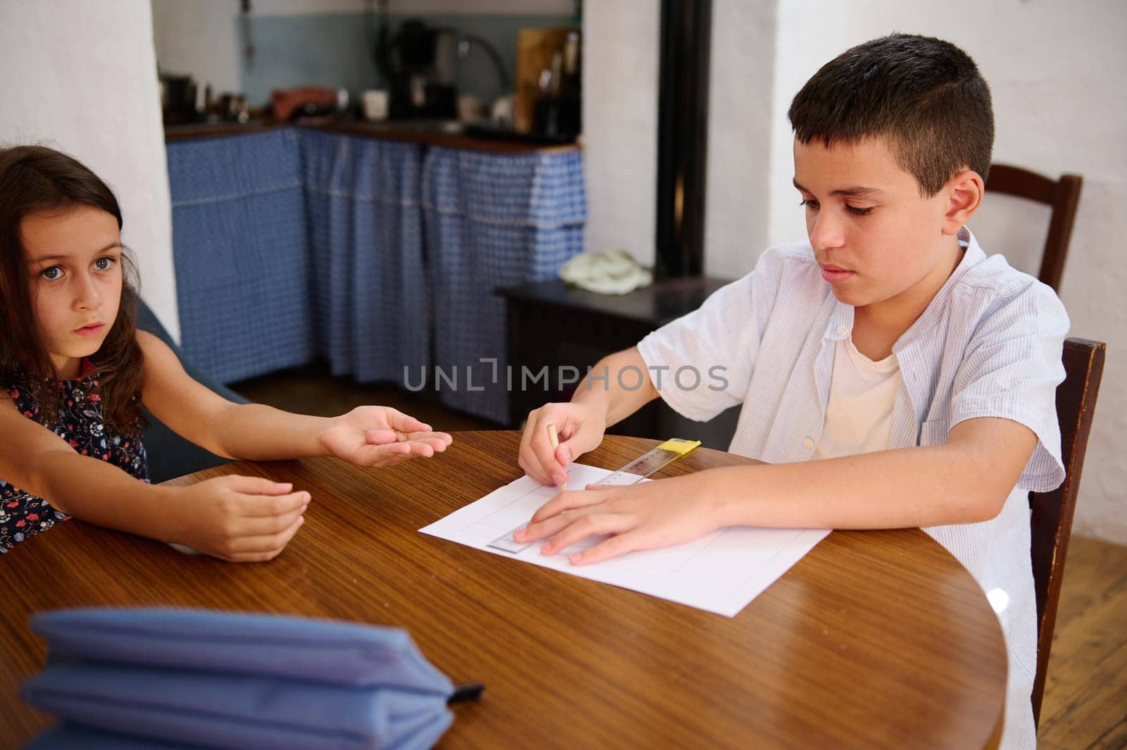 Two children work on an arts and crafts project at a wooden table, focused and creative.