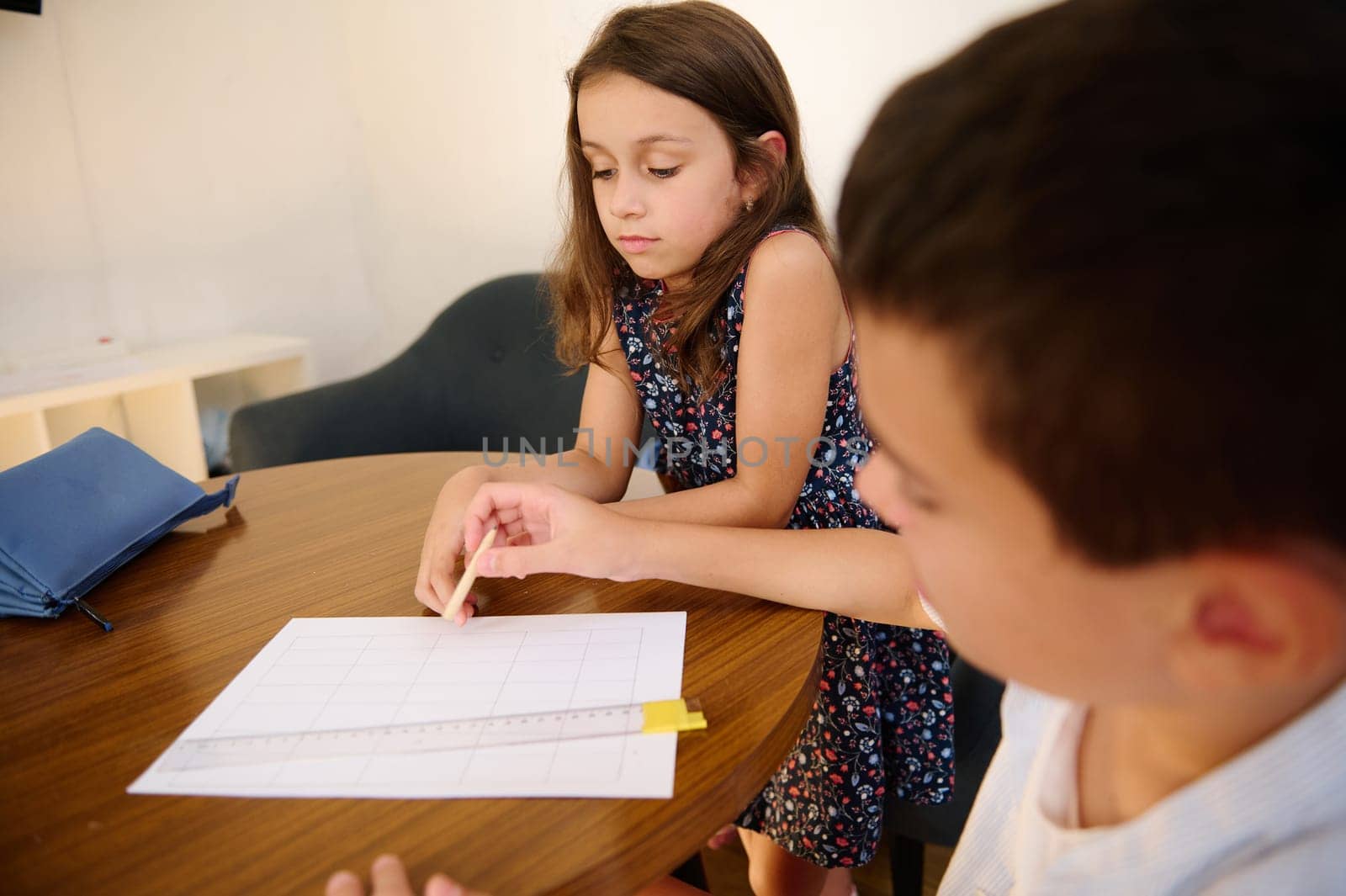 Two children collaborating on a worksheet together at a wooden table in a calm setting, focusing and sharing ideas.