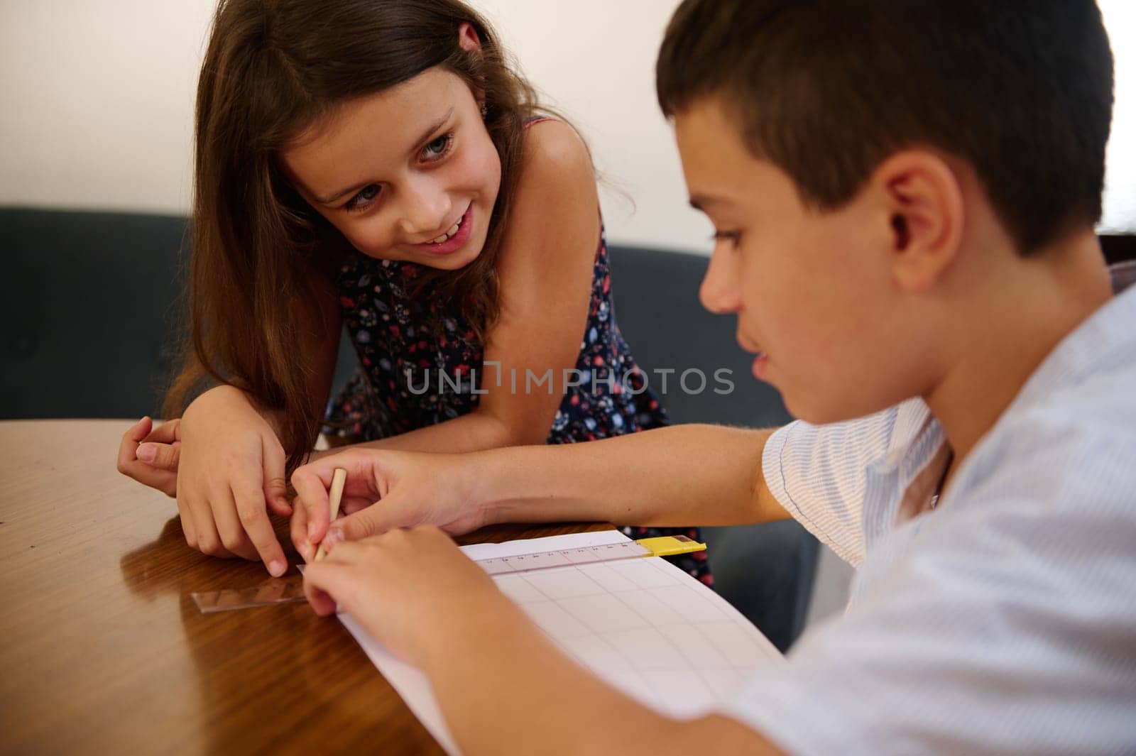 Two children collaborate on homework tasks at a table, promoting teamwork, focus, and learning. Their shared moment signifies friendship, support, and the joy of acquiring knowledge together.