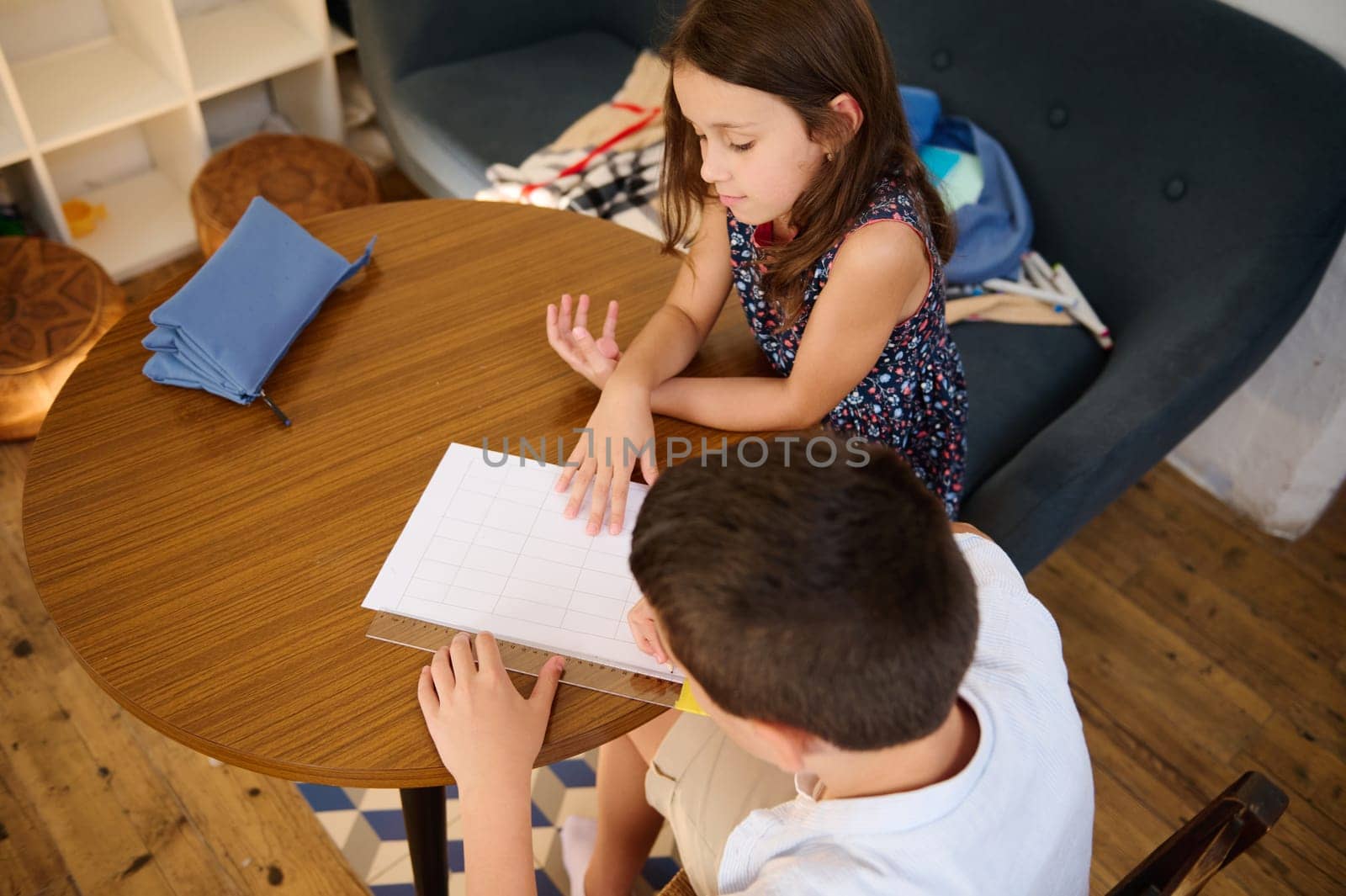 Two children engaged in studying while sitting indoors at a wooden table, fostering educational interaction.