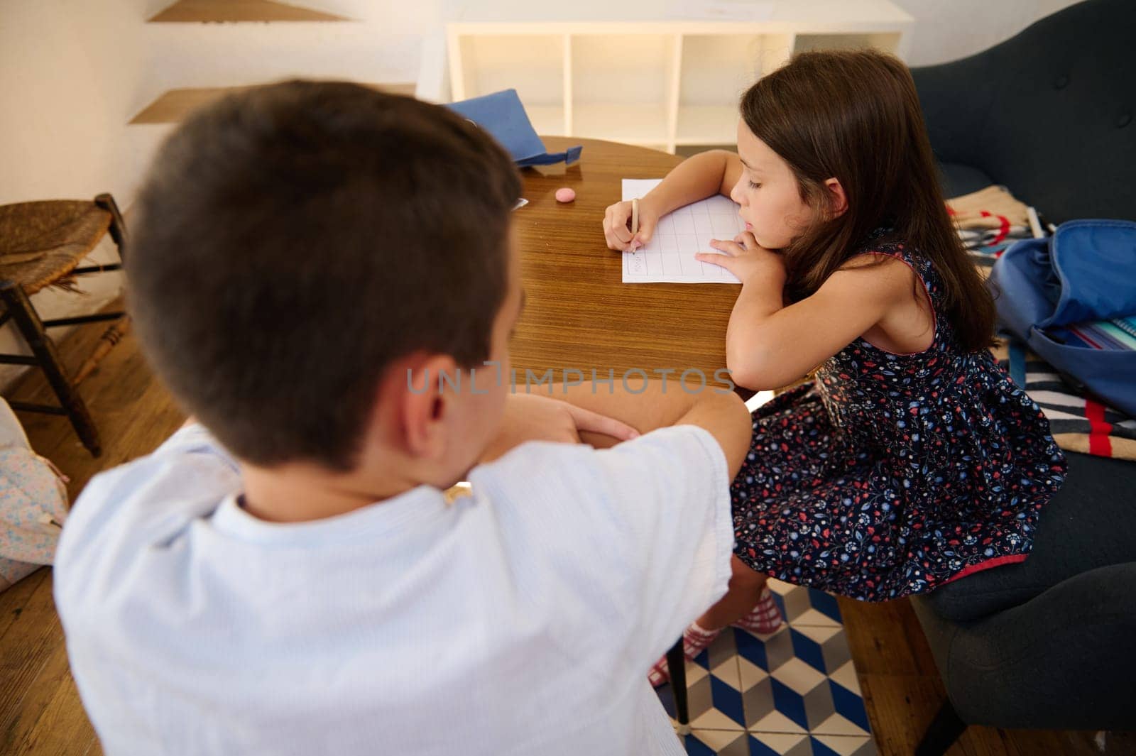 Young children sit at a table, focusing on writing and activities in a home environment, promoting education.