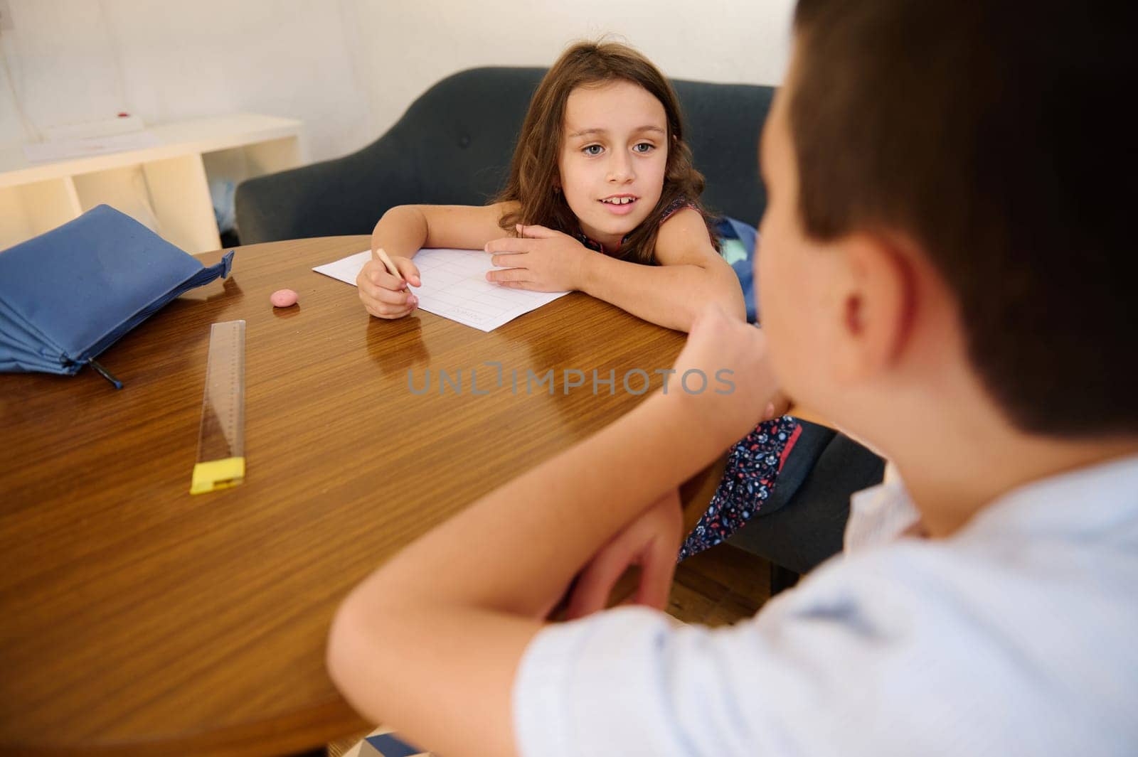 A young boy and a girl collaborate on schoolwork, sitting at a wooden table.