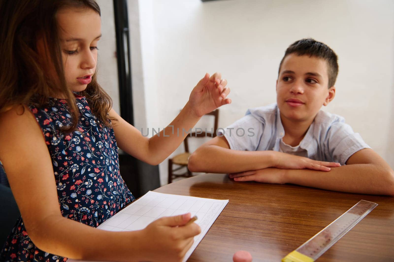 Two children are working together on an educational activity, sharing ideas and tools at a wooden table indoors.