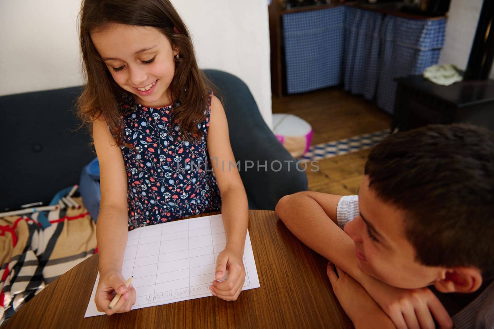 Two children are collaboratively working and sharing a good moment at home while solving homework, emphasizing education and teamwork.