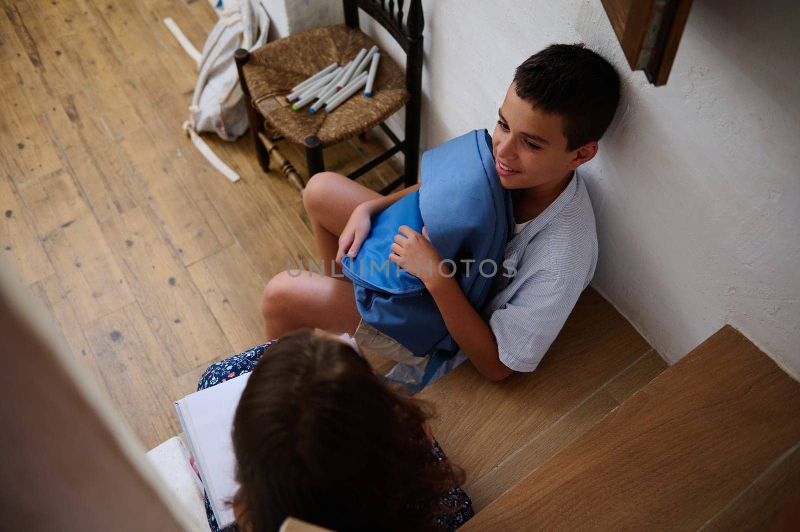 Two children engage in conversation while sitting on stairs, surrounded by school supplies. They appear to be on a break or studying together, demonstrating a sense of learning and friendship.