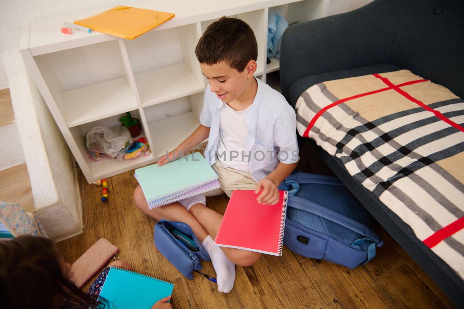 A young boy sits on the floor organizing school notebooks and supplies in a cozy room.