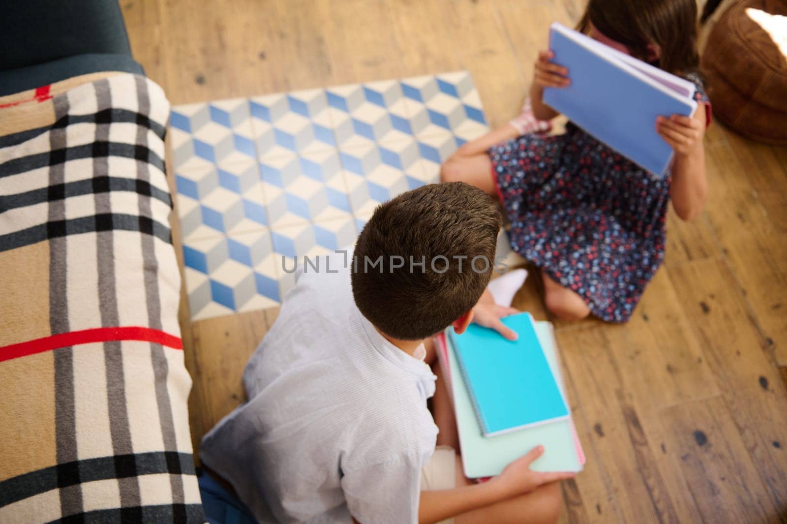 Two children engaged in learning activities, sitting on the wooden floor with notebooks.