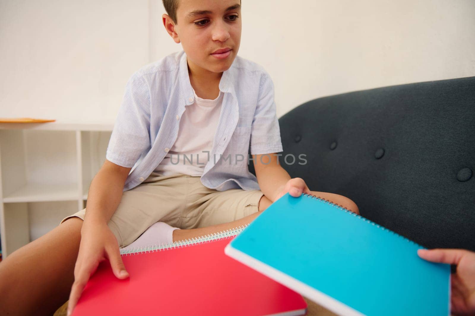A young boy sits holding colorful notebooks, looking thoughtful and focused, possibly engaged in a study or creative activity, highlighting education and learning moments.