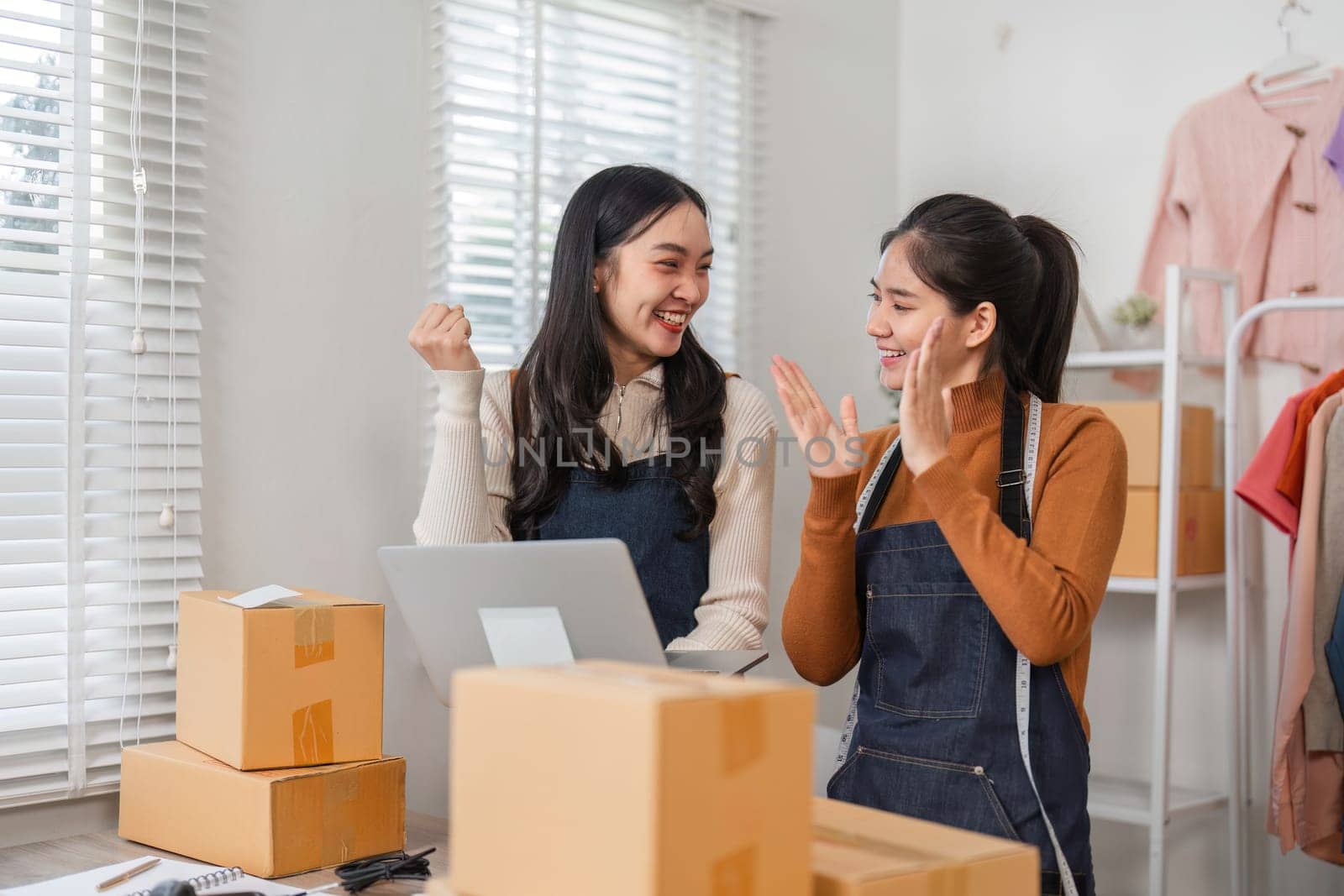 Two diverse female e-commerce employees celebrating successful sales and achievements while working in a retail store environment.