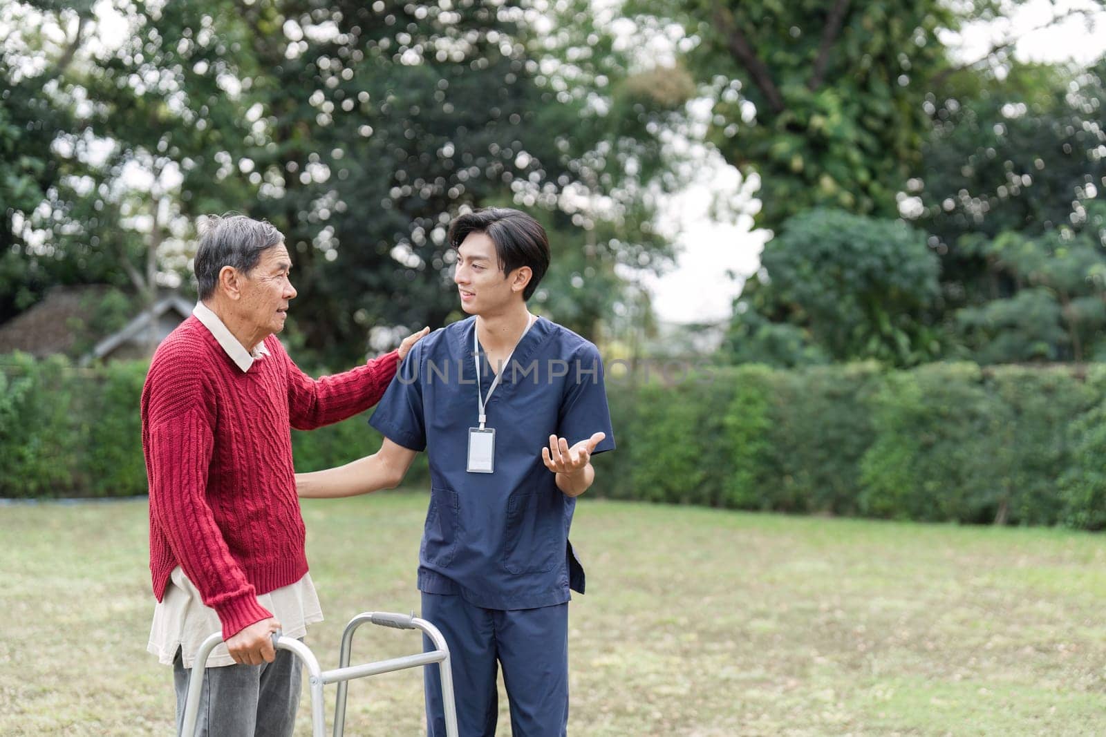 A caring healthcare professional speaks warmly with an elderly man using a walker, fostering connection and understanding in a serene outdoor setting.