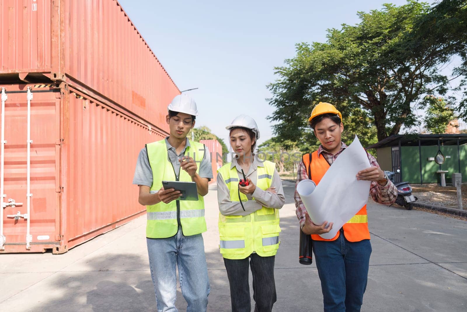 Three construction professionals, including an engineer, a project manager, and a worker, collaborating using blueprints and a tablet at a vibrant construction site.