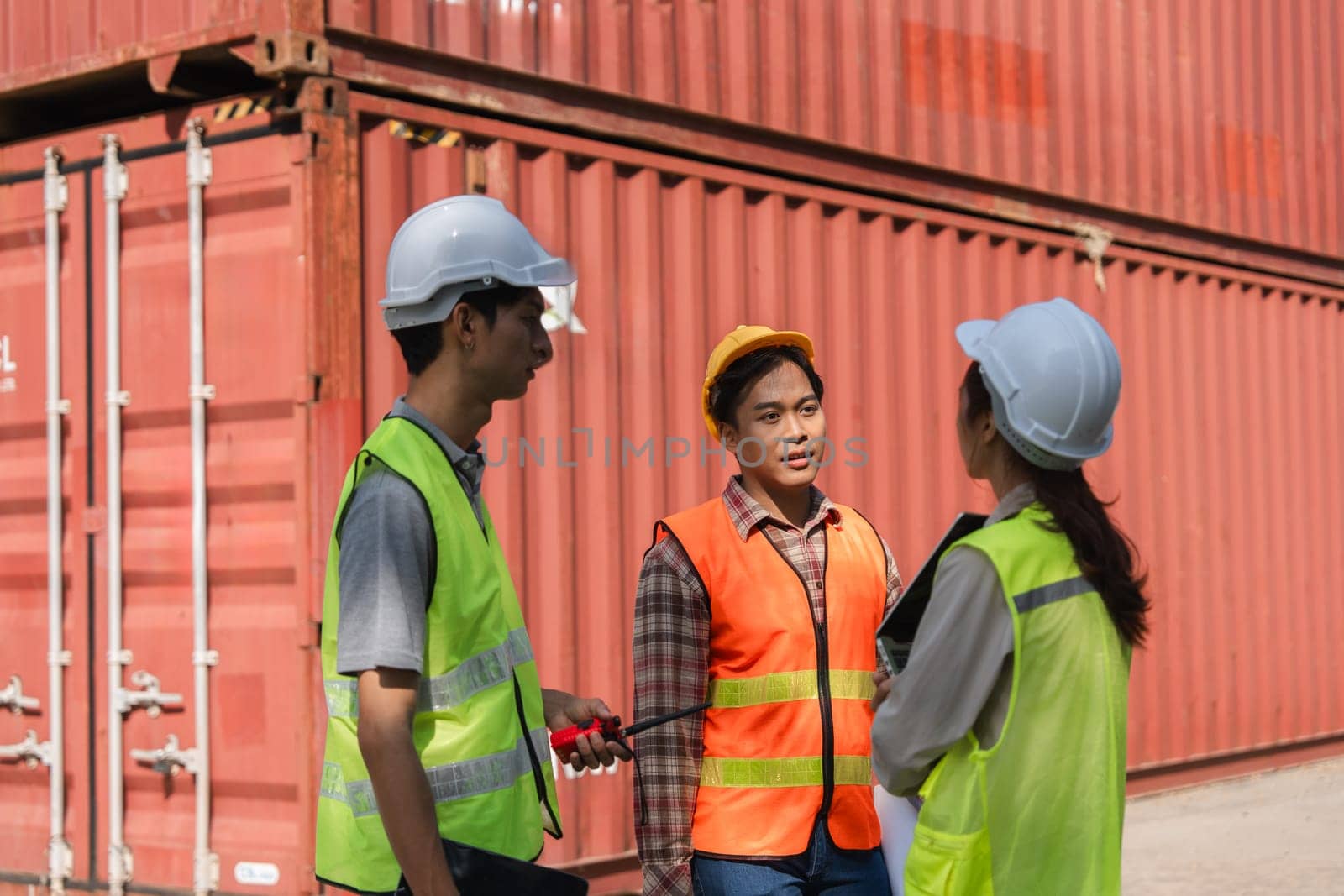 A group of construction professionals, including a female engineer and a male supervisor, actively discussing safety measures near shipping containers at the construction site.
