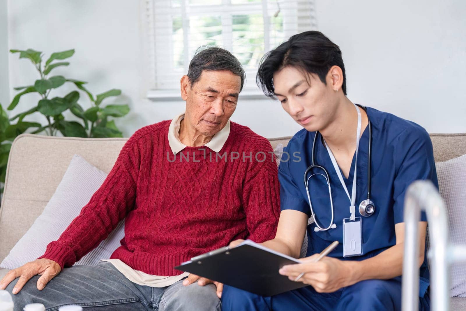 A thoughtful nurse records essential health information as an elderly man attentively listens, fostering effective communication in a home care environment.