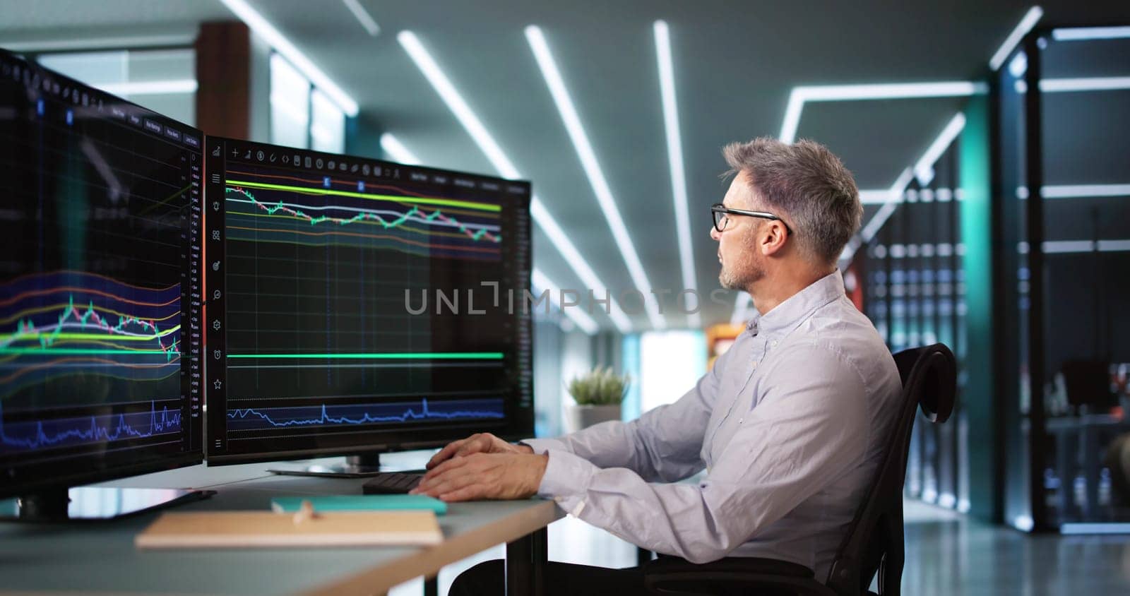 Stock Market Broker Looking At Graphs On Multiple Screens In Office