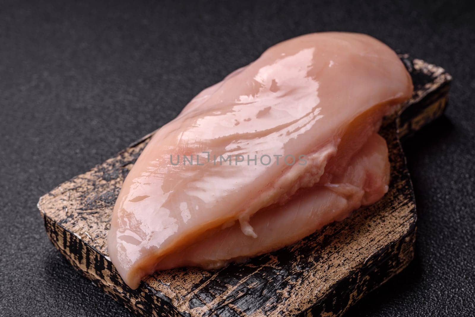 Raw chicken or turkey fillet with salt, spices and herbs on a dark concrete background