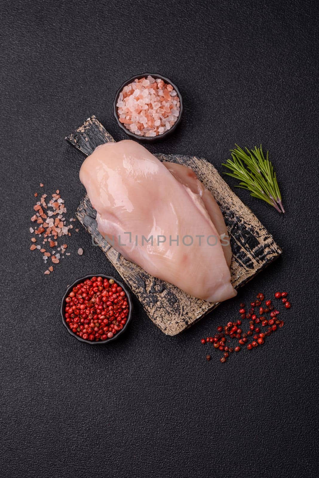 Raw chicken or turkey fillet with salt, spices and herbs on a dark concrete background