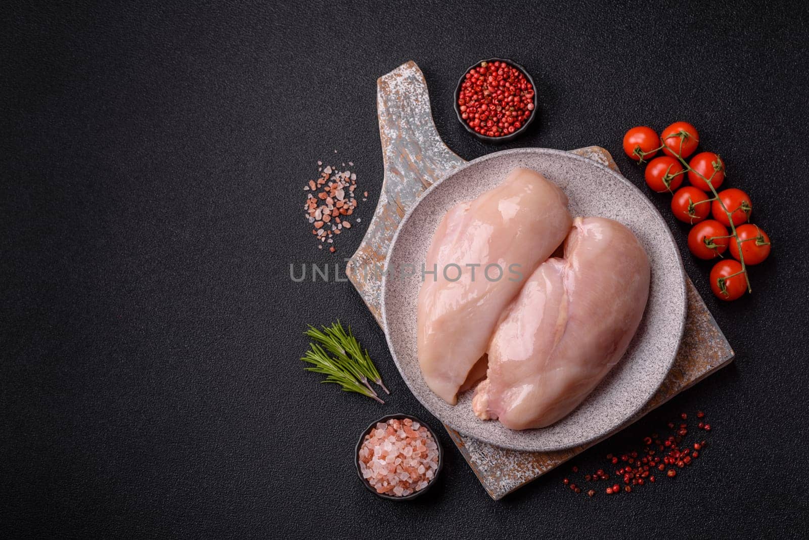 Raw chicken or turkey fillet with salt, spices and herbs on a dark concrete background