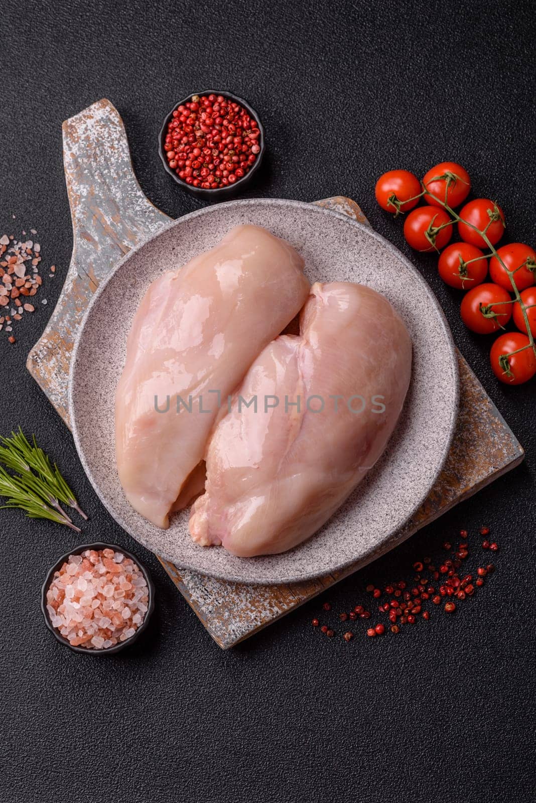Raw chicken or turkey fillet with salt, spices and herbs on a dark concrete background