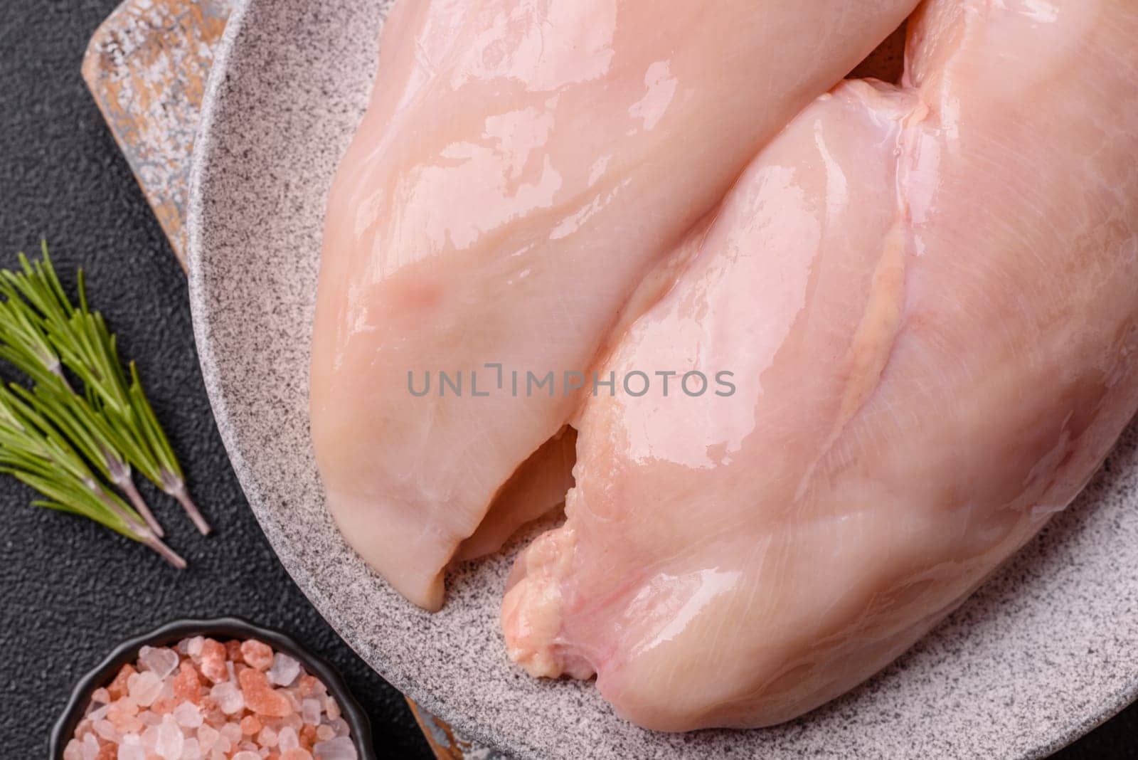 Raw chicken or turkey fillet with salt, spices and herbs on a dark concrete background