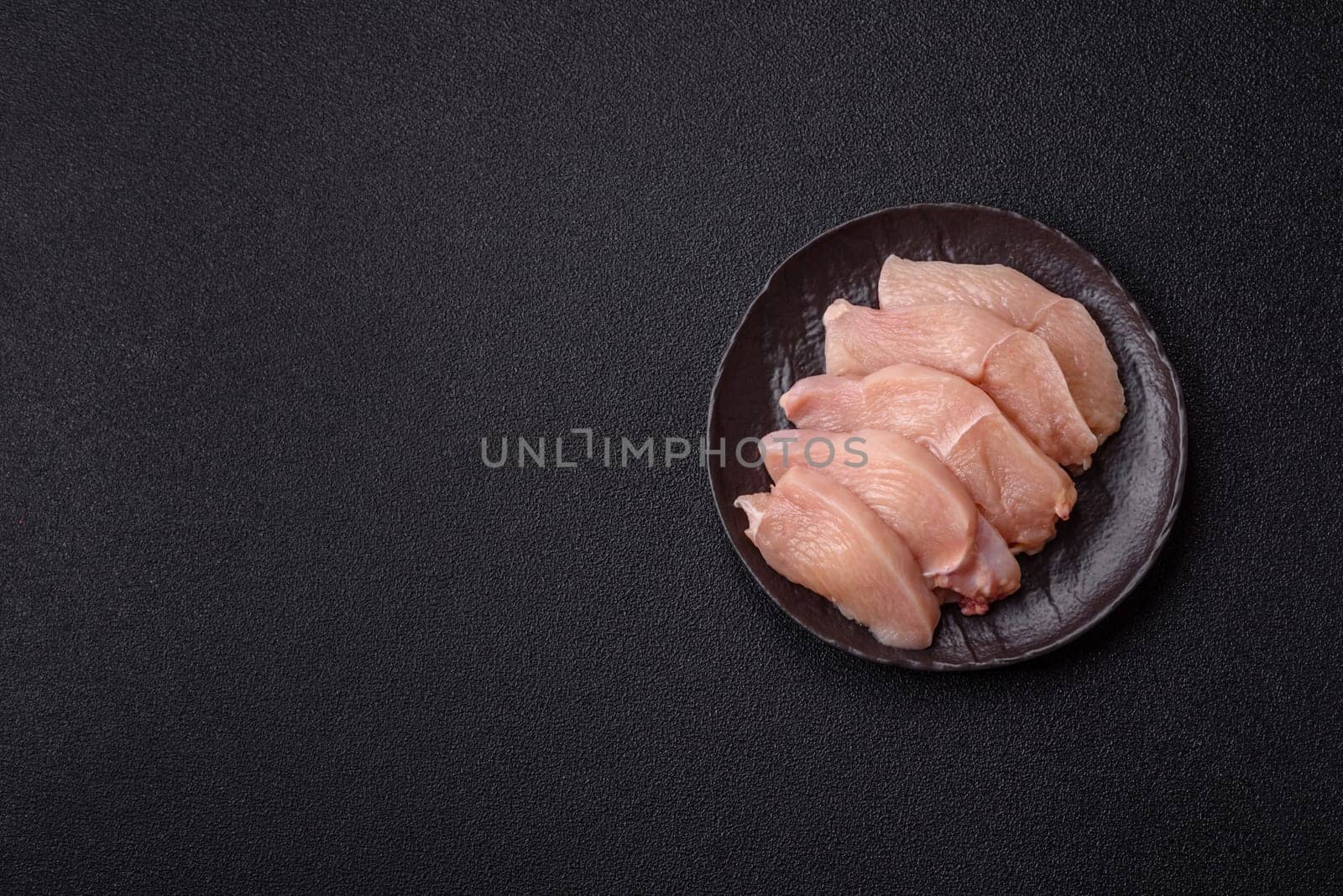 Raw chicken or turkey fillet cut into slices with salt, spices and herbs on a dark concrete background