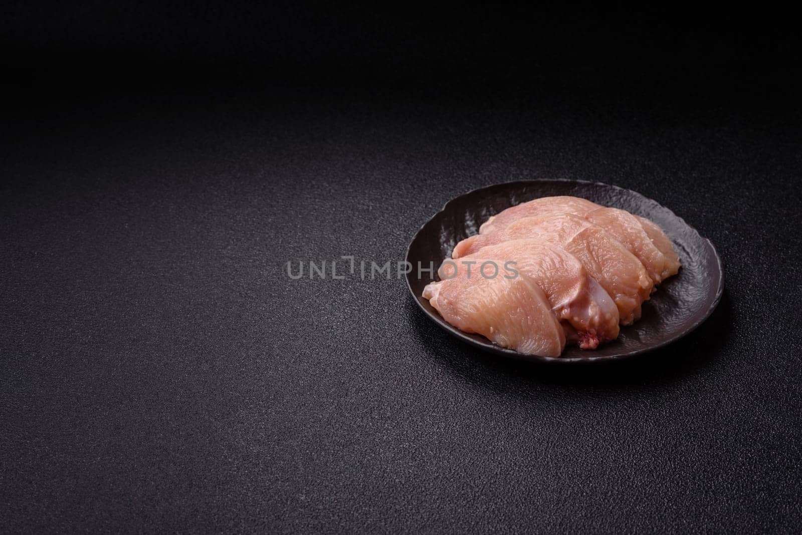 Raw chicken or turkey fillet cut into slices with salt, spices and herbs on a dark concrete background