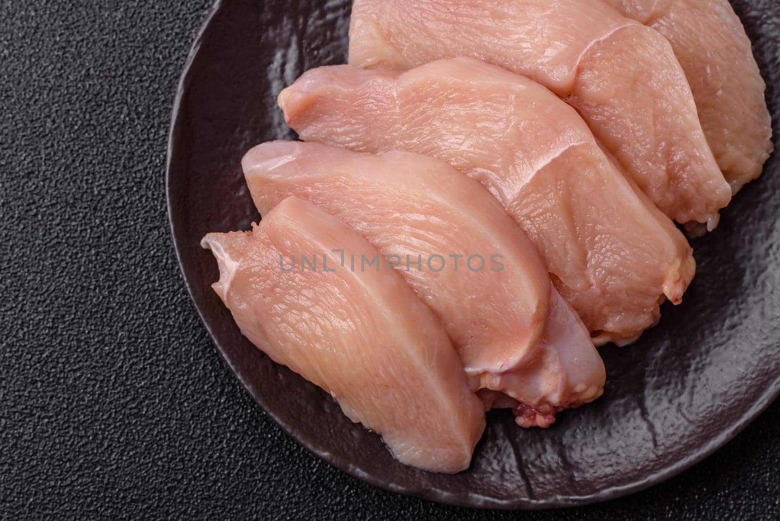 Raw chicken or turkey fillet cut into slices with salt, spices and herbs on a dark concrete background