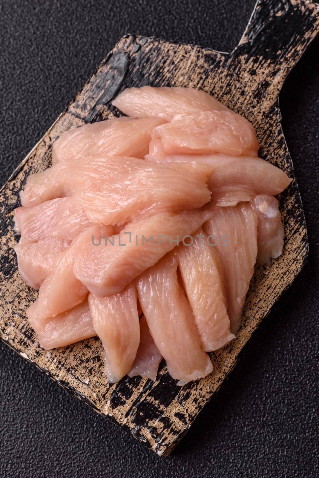 Raw chicken or turkey fillet cut into slices with salt, spices and herbs on a dark concrete background