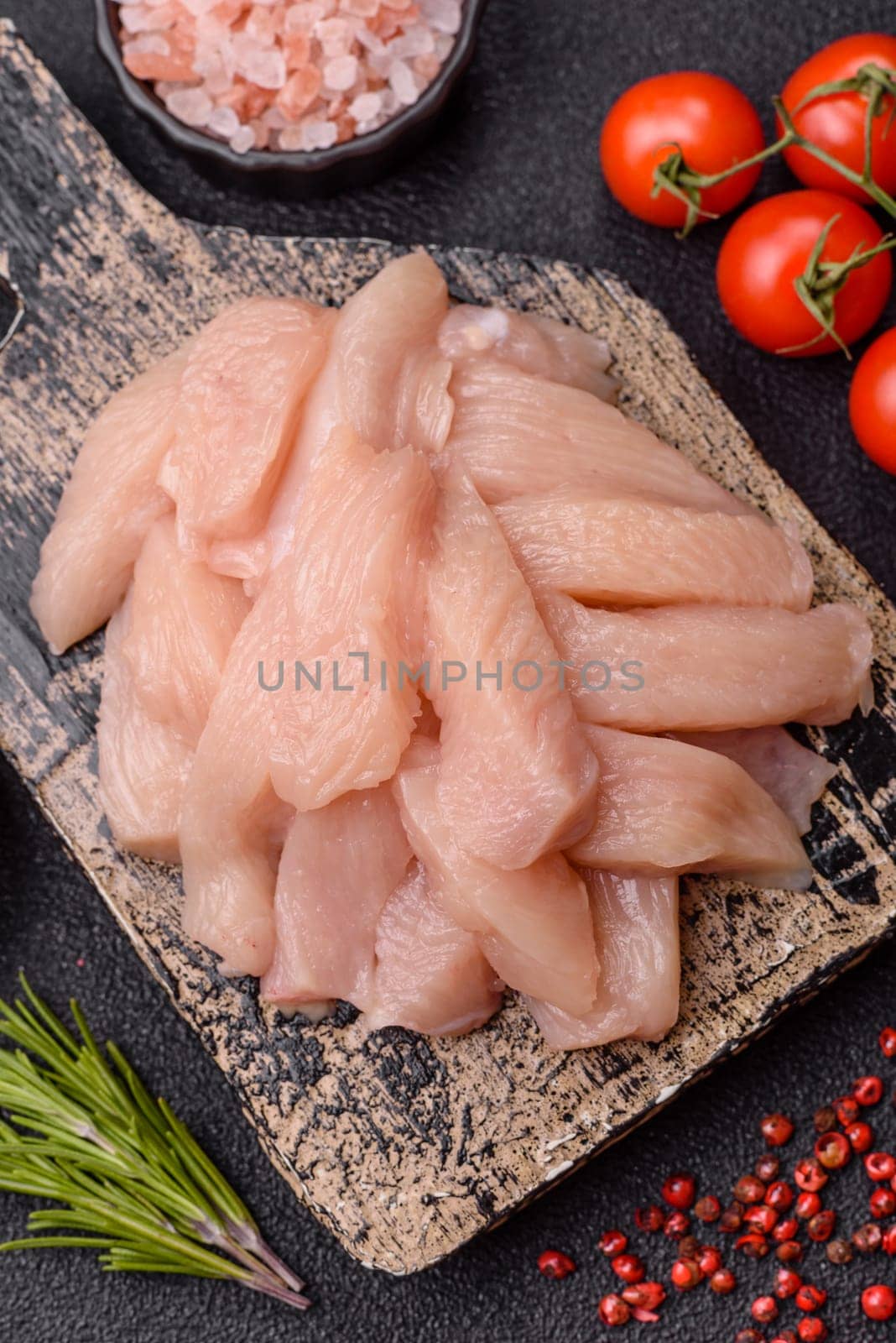 Raw chicken or turkey fillet cut into slices with salt, spices and herbs on a dark concrete background