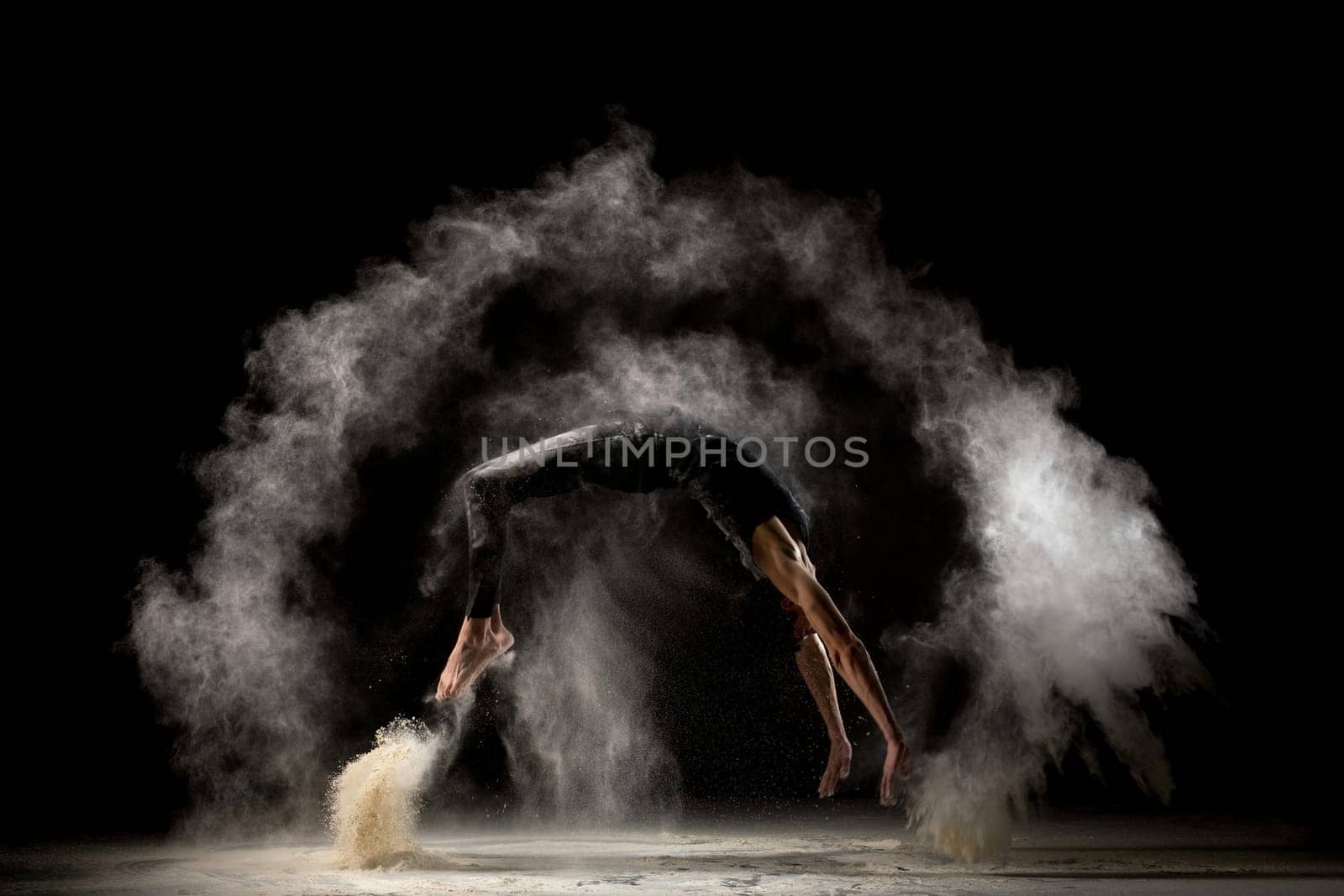 Male gymnast jumping in white dust cloud profile view in the dark room