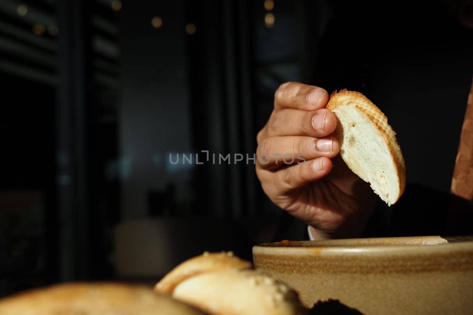 A hand reaches for a slice of bread to dip into a flavorful sauce.