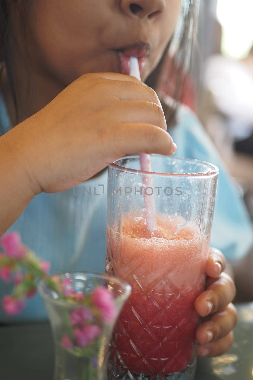 A young person sips a colorful drink through a straw while seated.