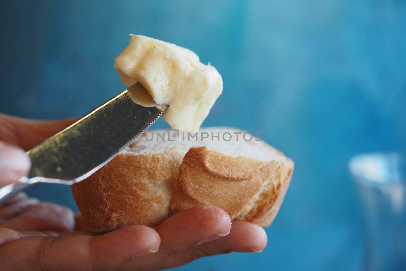 A hand applies soft butter on a slice of bread against a blue background.