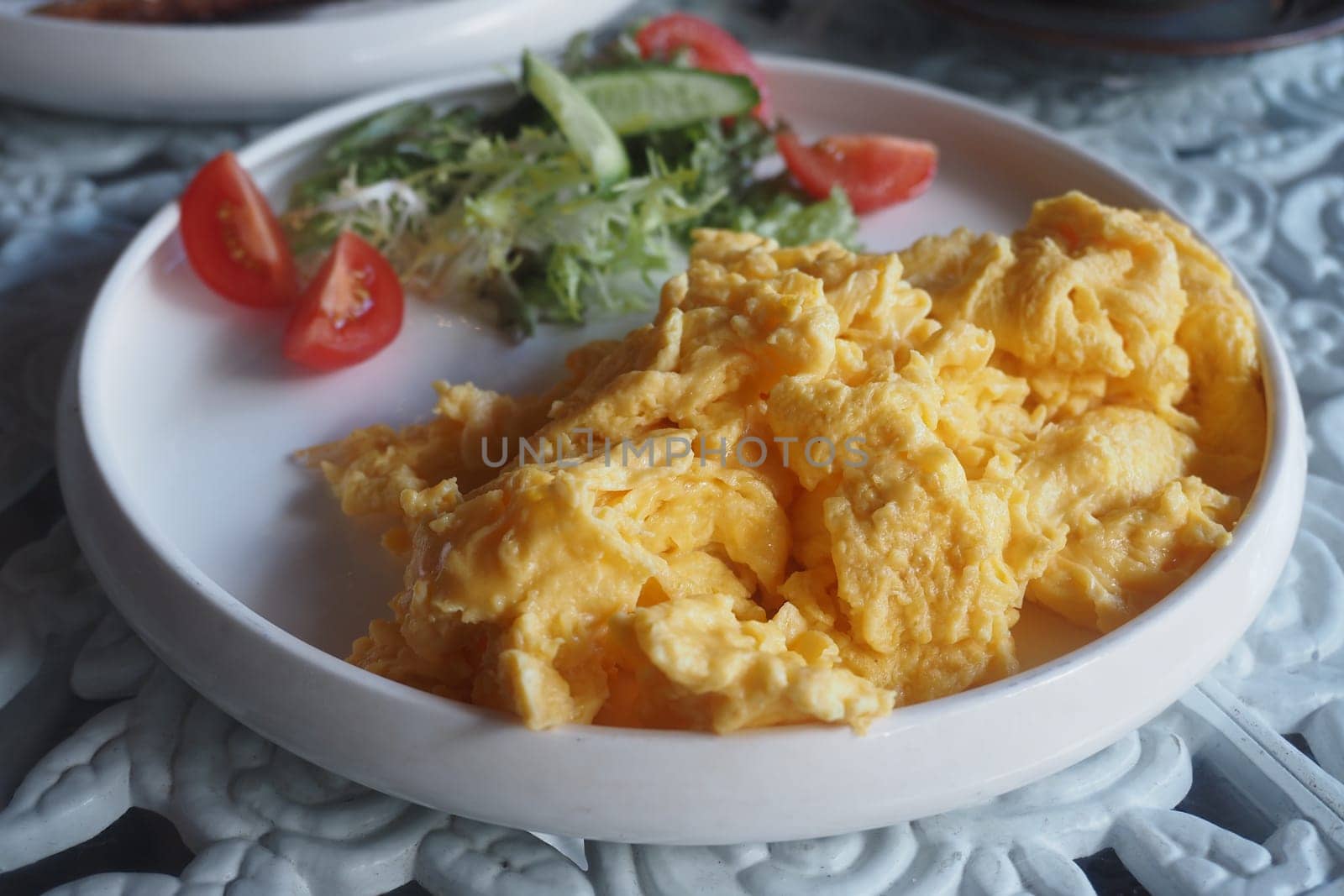 Soft scrambled eggs are plated alongside tomatoes and greens.