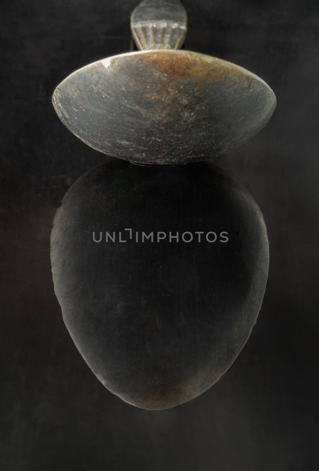 Reflection on a black surface of Old ancient worn vintage spoon in close up an oval is shaped like an egg. Curve details of Black metal vintage spoon in dark tone, Highlighting its texture and design, use it as your Space for text, Design, Wallpaper and Poster, Selective focus.
