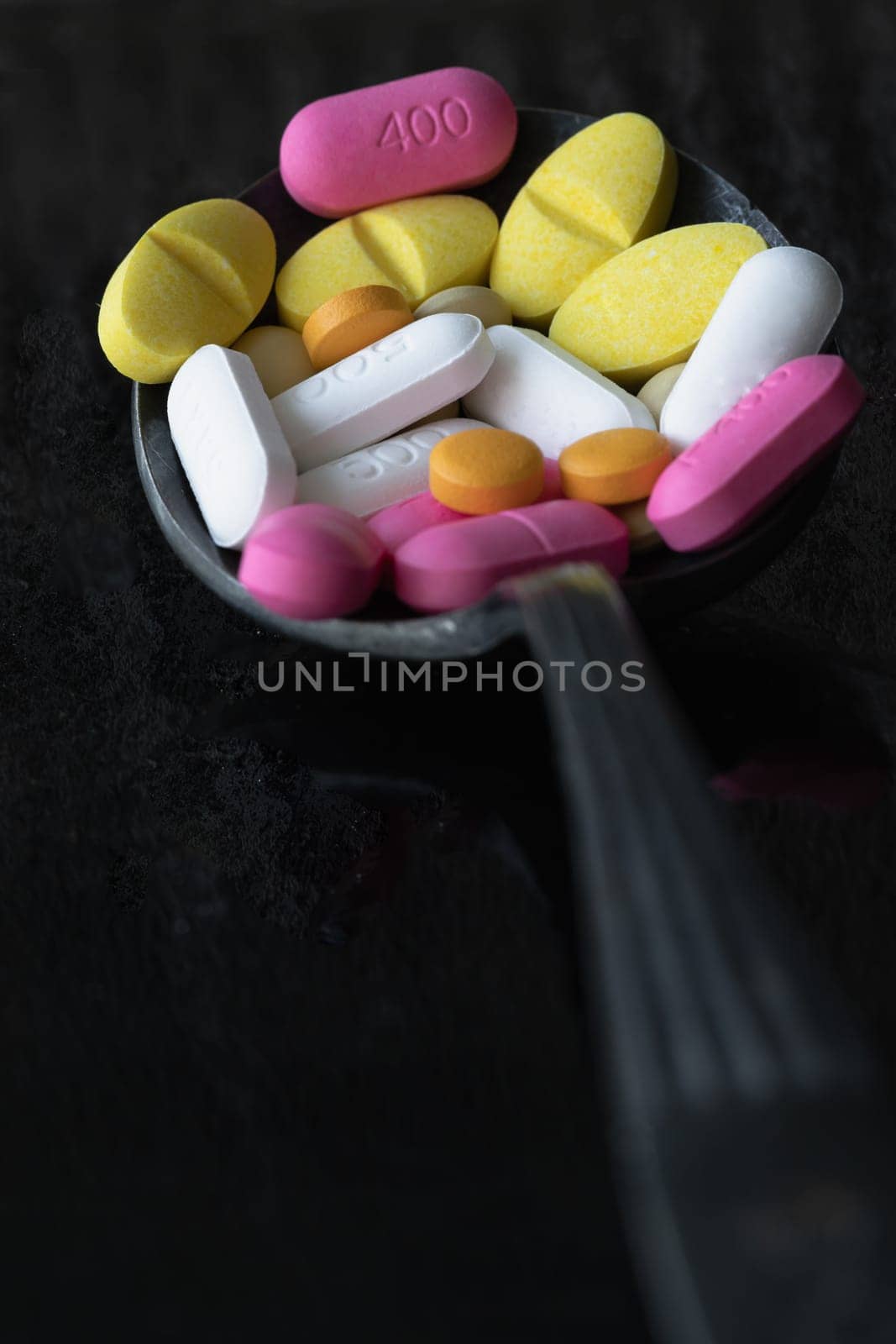 Perspective view of A lot of pills of different colors and shapes on Ancient vintage spoon isolated on black background. Concept of medication treatment and Health care, use it as your Space for text, Design, Wallpaper and Poster, Selective focus.