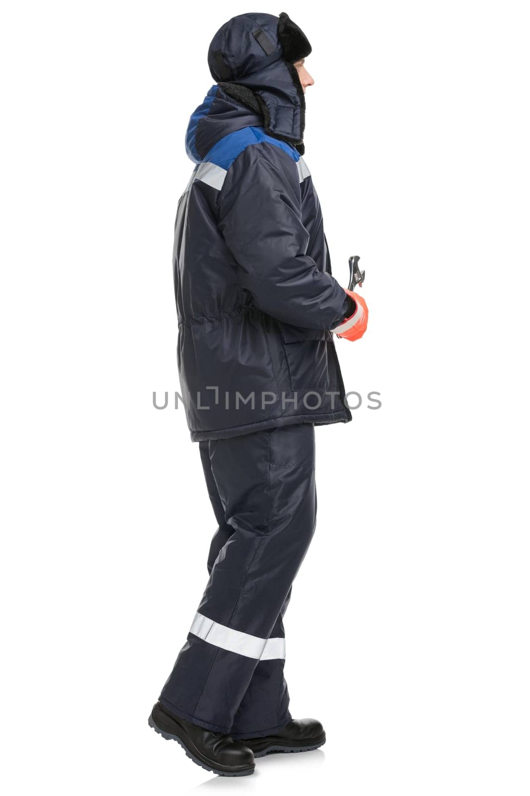 Side view of man in warm blue trousers and jacket with reflective inserts hat on head and wrench in hand isolated on white background