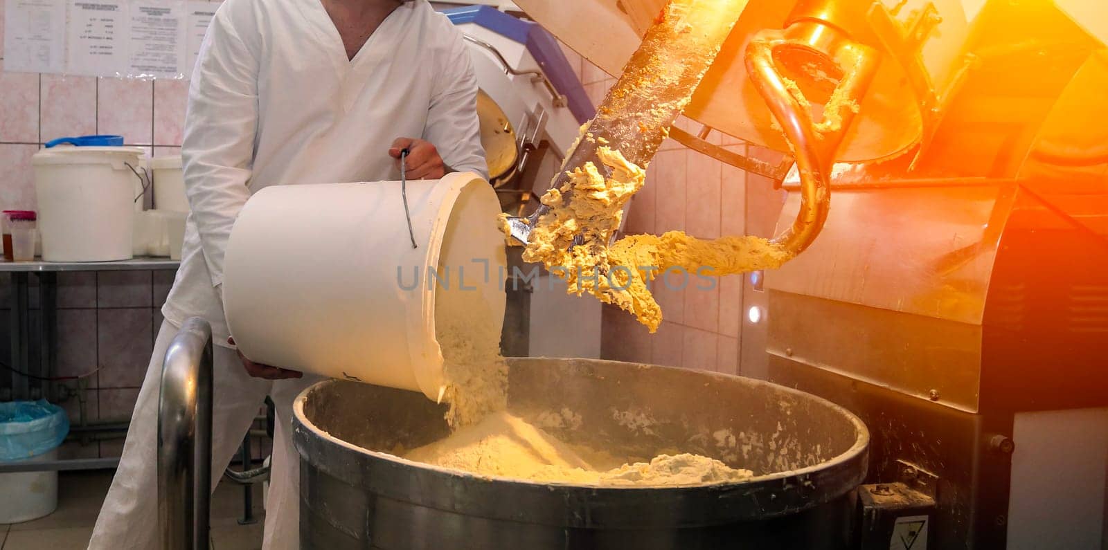 A dedicated worker adds ingredients to a large mixer, creating dough for delicious biscuits in a bustling factory during production hours.