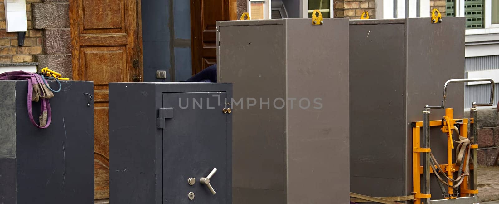 Several large safes are being moved outside a building, with workers organizing equipment in a bustling urban area.