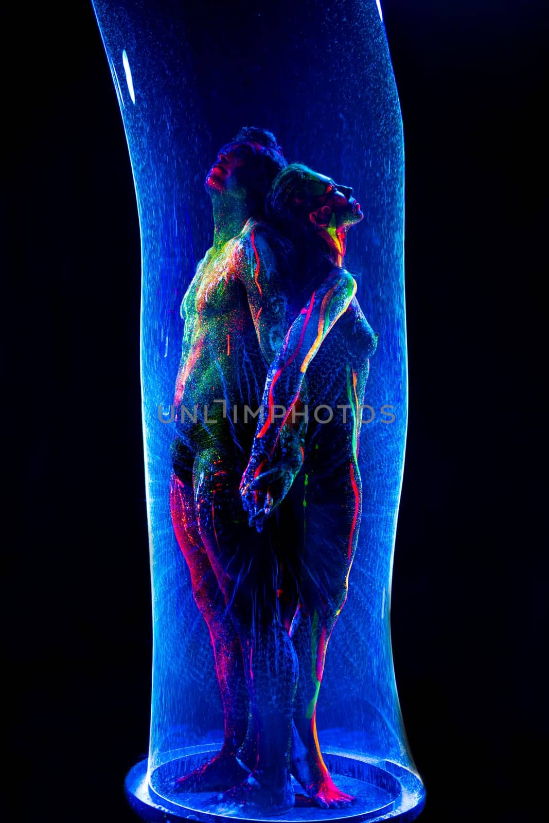 Naked man and woman with colorful fluorescent body art standing in glow bubble tube